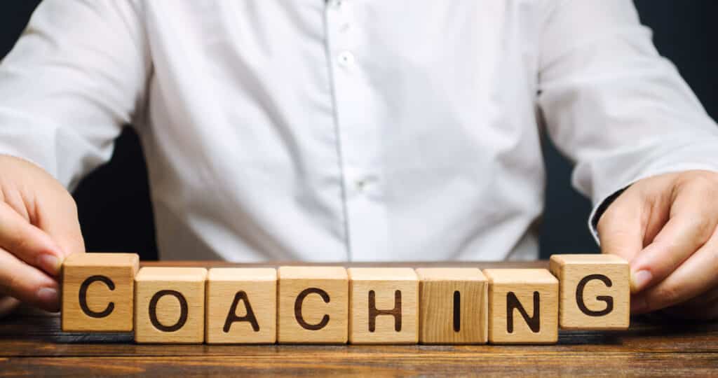 Wooden blocks with the word Coaching in the hands of a man. 