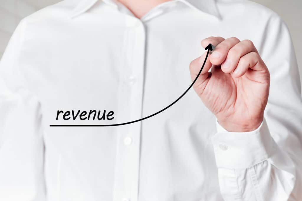 Businessman with a pen draws a rising line graph with the word revenue on a virtual screen. Business revenue increase concept.