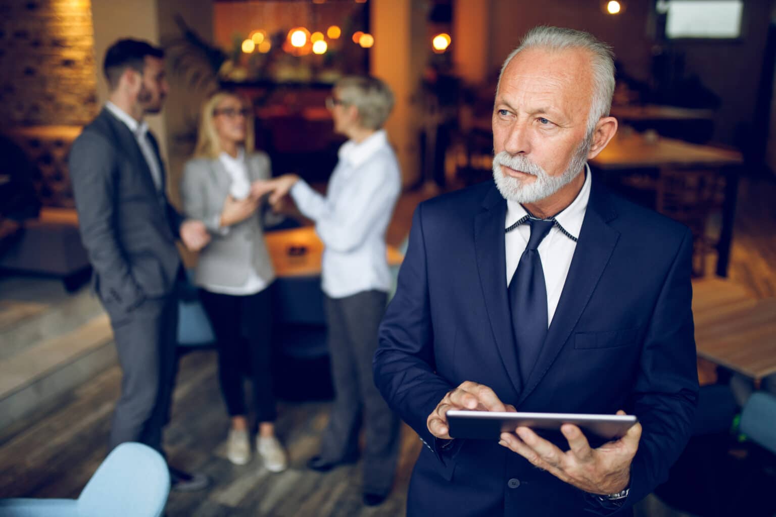 Successful businessman using digital tablet with his family business colleagues in the background.