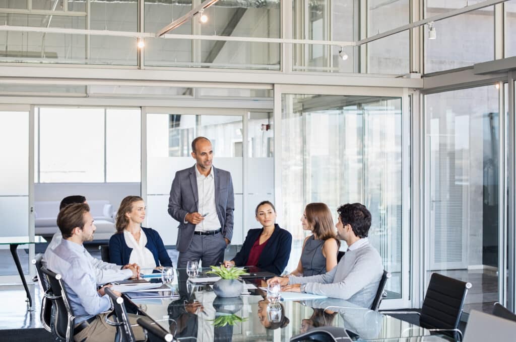 Digital transformation coach talking with a group of businesspeople sitting in a conference room.