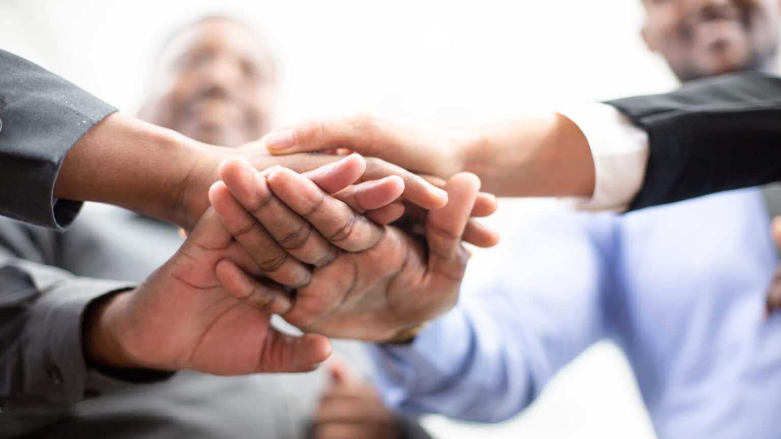 United coworkers standing with their hands together in modern office, celebrating victory, teambuilding and unity