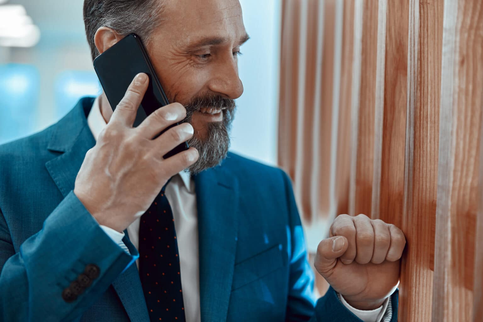 Close up of smiling business man in suit standing in the office space and talking on the phone with an executive coach