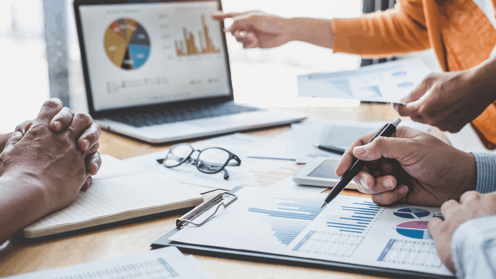 Business professionals reviewing charts and financial data on paper and a laptop during a strategy planning meeting.