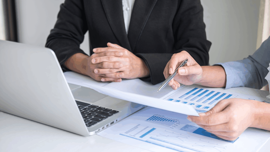 Close-up of two professionals reviewing charts and reports together at a laptop, discussing performance metrics and business strategy.