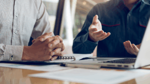 Two business professionals meeting to discuss strategic business planning with a business strategy consultant, reviewing notes and a laptop.