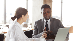 Two professionals engaged in a focused CEO coaching session at a modern office, discussing leadership strategies with a laptop on the table.