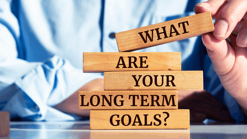 Hand arranging wooden blocks with the inscription “What are your long term goals?” in a motivational setting.