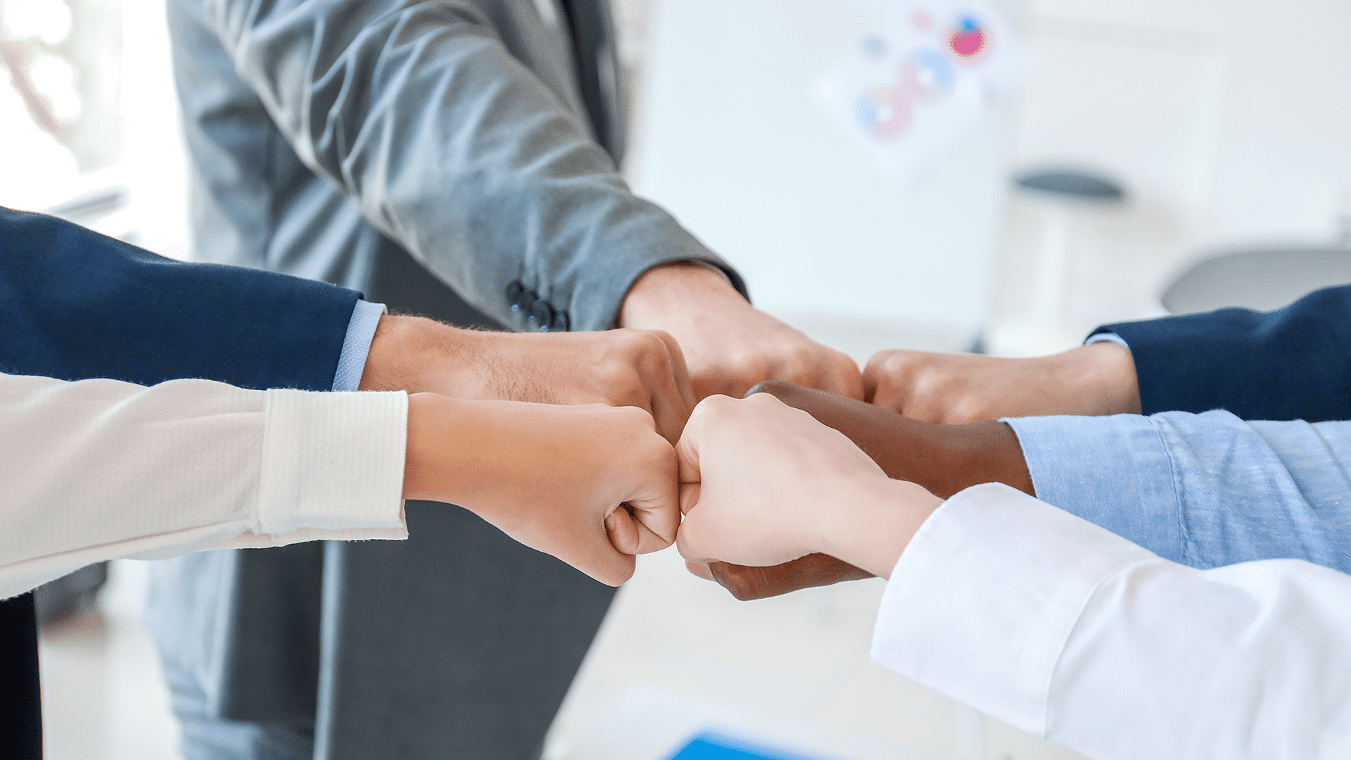 Diverse group of business professionals joining fists together in a circle, symbolizing teamwork and unity.