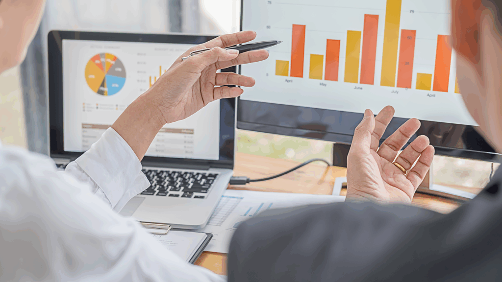 Two professionals analyzing data and charts on computer screens during a business meeting.