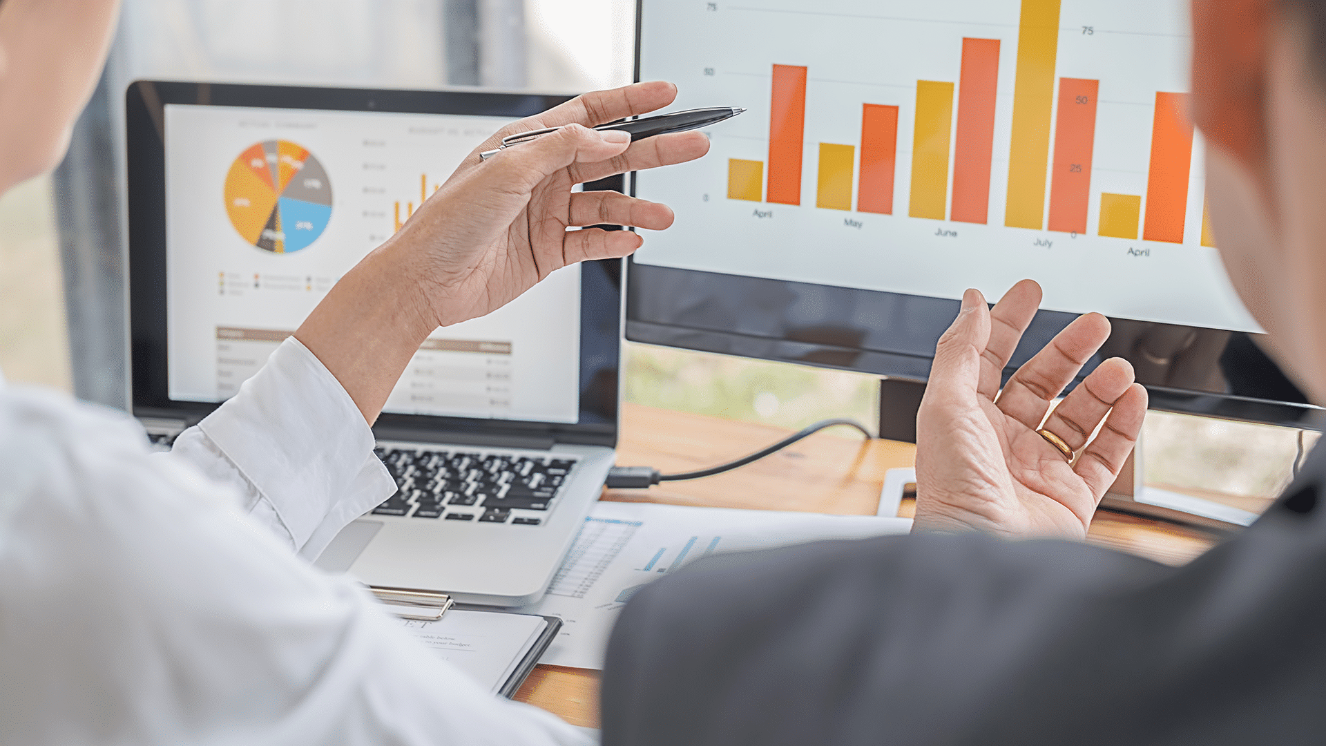 Two professionals analyzing data and charts on computer screens during a business meeting.