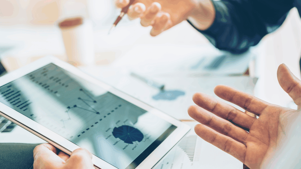 Hands of professionals discussing data visualizations and charts displayed on a digital tablet during a business meeting.